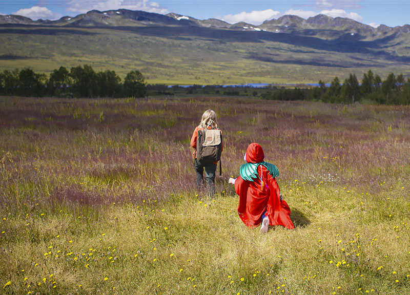 Die beiden Mädchen wandern durch eine weite Graslandschaft mit Bergen im Hintergrund