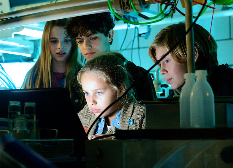 Die Kinder stehen in einem dunklen Raum hinter Clarissa, die auf einen Computerbildschirm starrt