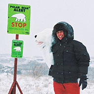 Willi in dicker Winterjacke in der Antarktis neben einem grünen Schild, das vor Eisbären warnt