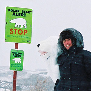 Willi in der Arktis neben einem Schild, das vor Eisbären warnt