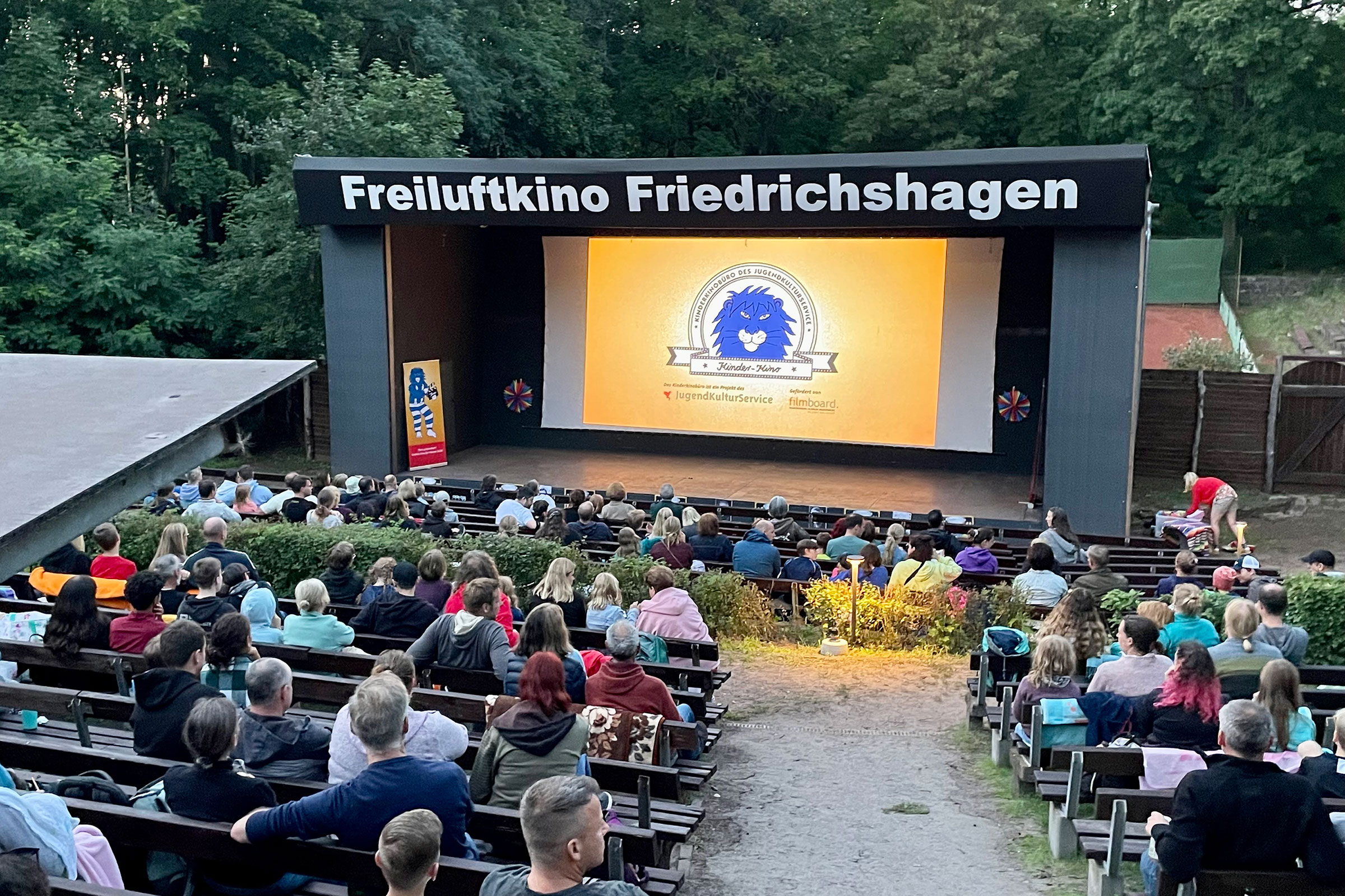 Publikum im Freiluftkino Friedrichshagen, auf der Leinwand läuft der Kinderkinobüro-Theo-Trailer