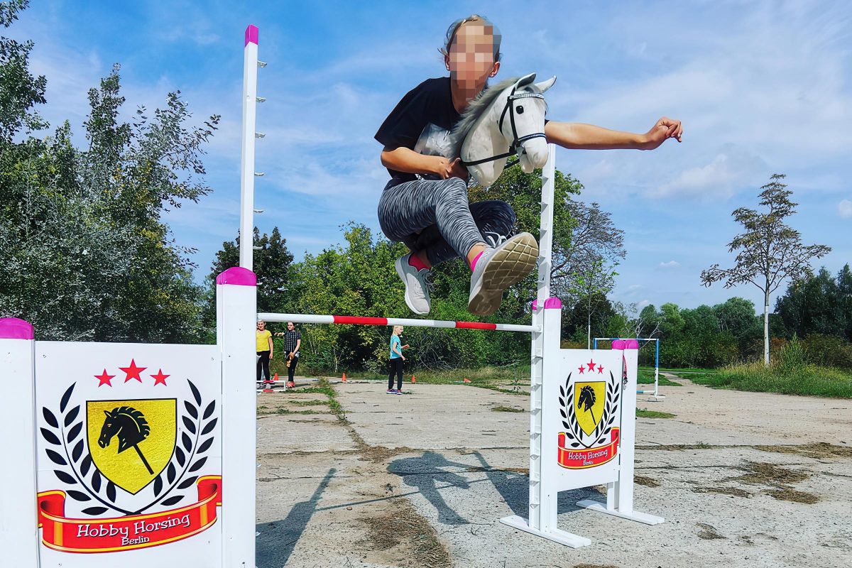 Ein Mädchen springt mit einem Steckenpferd über ein Hindernis auf einem Trainingsplatz