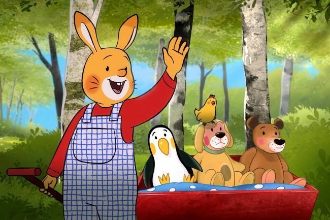 Karlchen steht im Wald und winkt. Im Bollerwagen sitzen seine Kuscheltiere Teddy, Hund und Pinguin