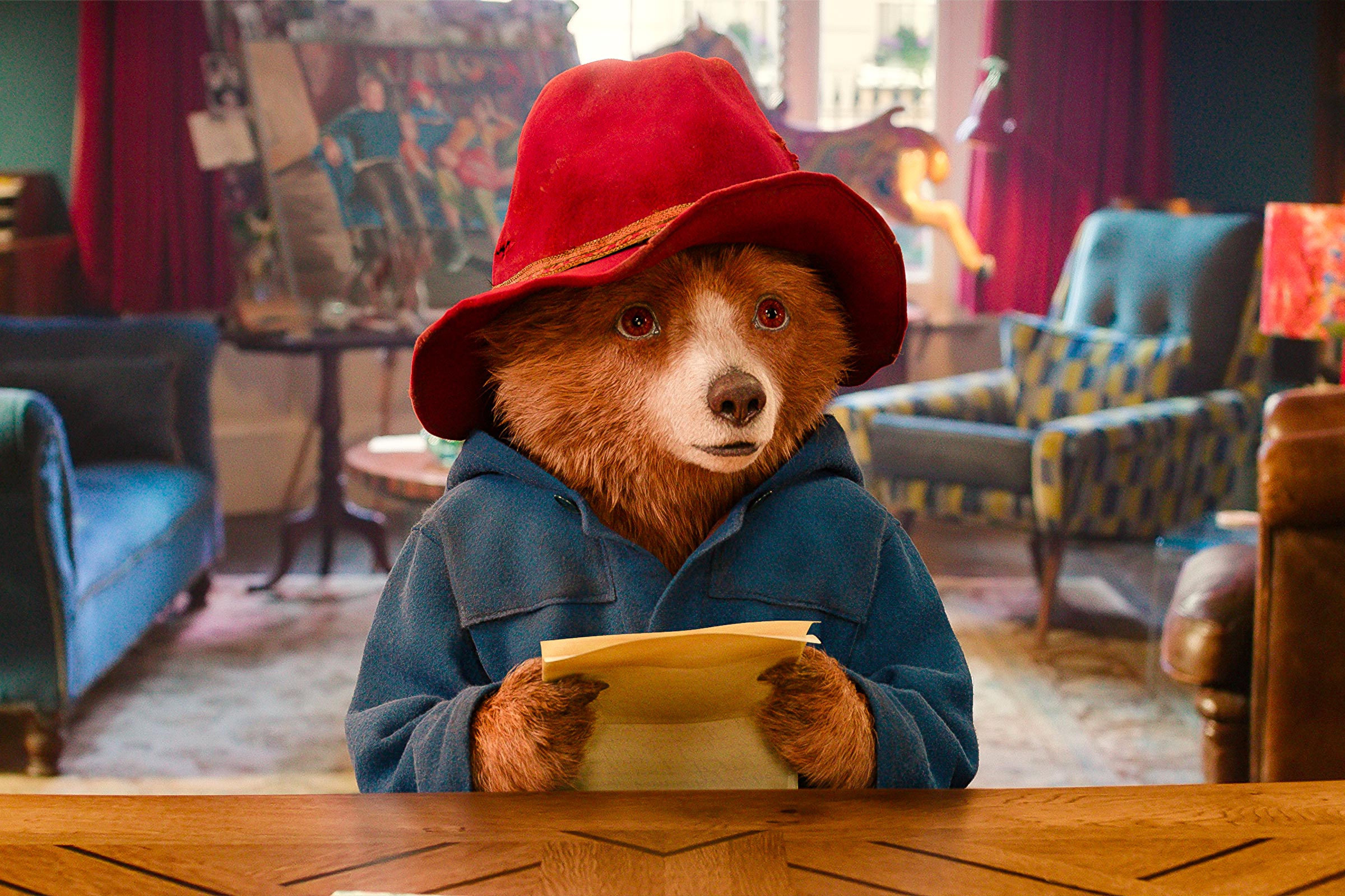 Paddington sitzt im Wohnzimmer und liest einen Brief
