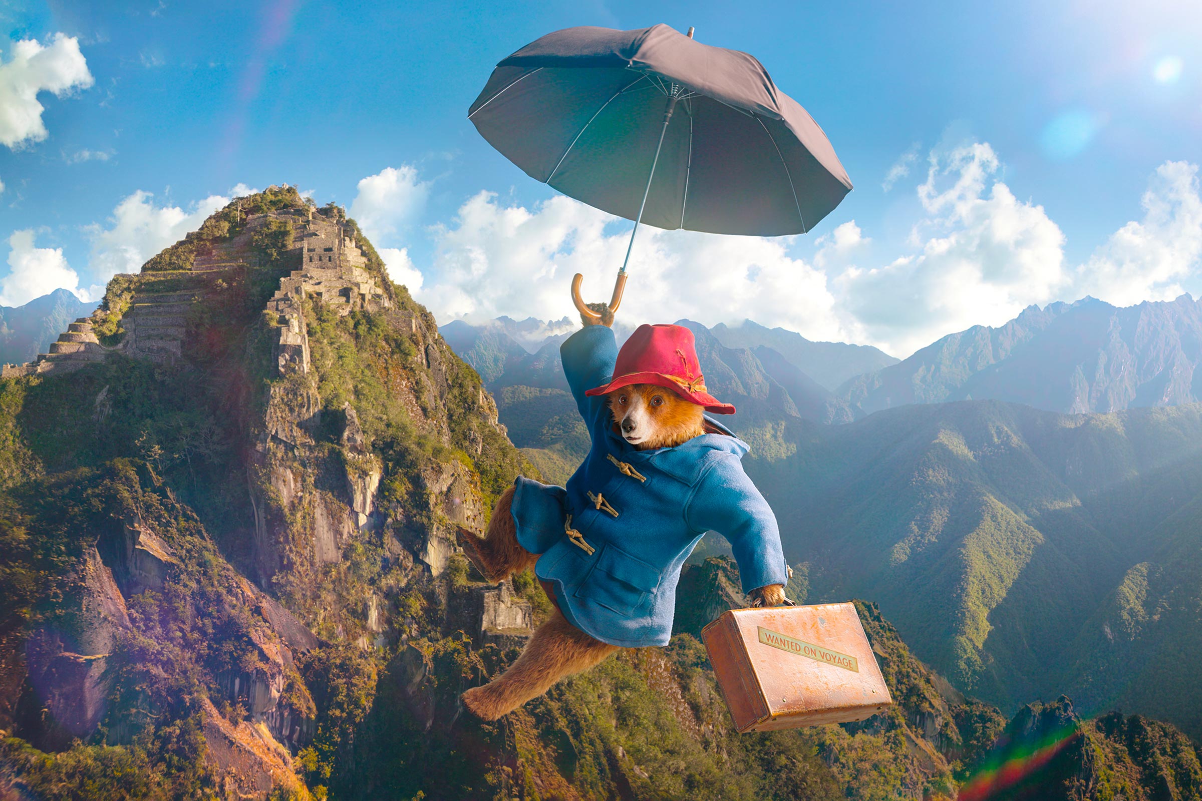 Der Bär Paddington fliegt mit seinem Schirm und einem Koffer über die Anden