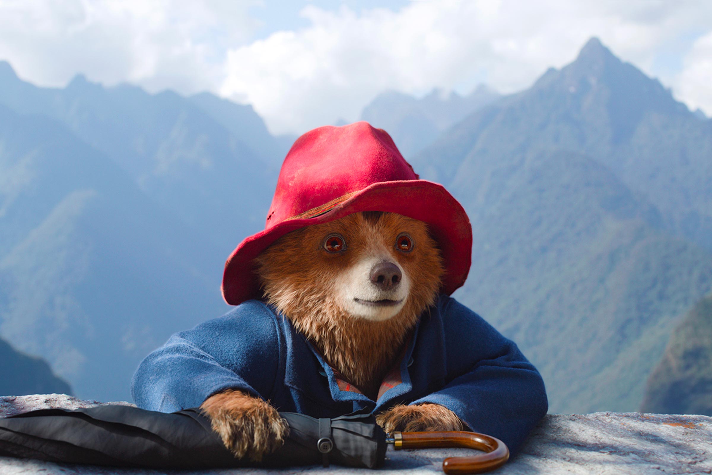 Der Bär Paddington schaut über eine Steinbrüstung, hinter ihm die Gipfel der Berge