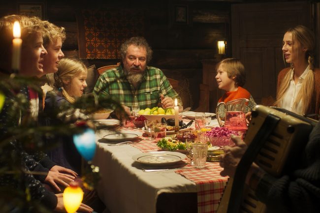 Die ganze Familie sitzt Weihnachten bei Kerzenlicht um den mit Speisen festlich gedeckten Tisch